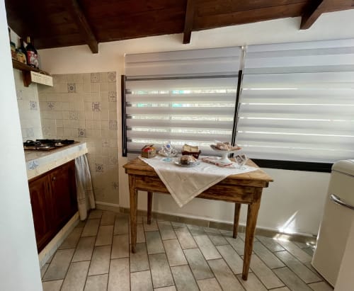 Cuisine de l'Appartement Il Soppalco à l'Agritourisme Stecadò, Dolceacqua, avec table en bois, cuisinière et fenêtre avec stores