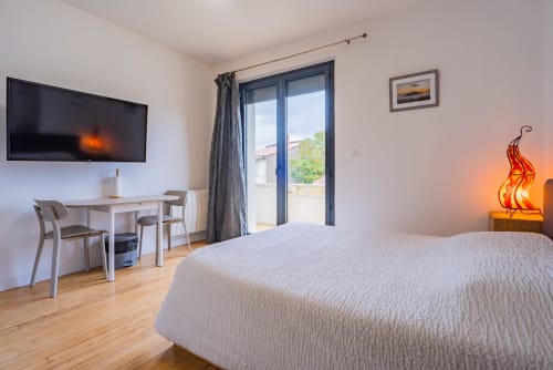 Chambre moderne dans un appartement toulousain avec lit double, bureau, télévision et balcon avec vue sur la ville