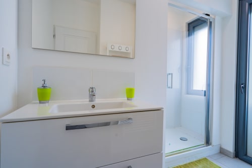 Salle de bain moderne dans un appartement toulousain avec vasque blanche, accessoires vert citron et douche vitrée