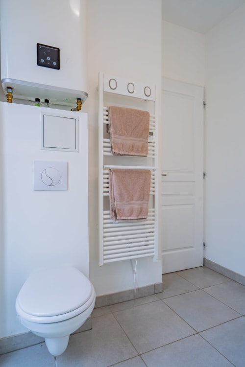 Salle de bain moderne blanche avec radiateur sèche-serviettes mural, bidet et chauffage de serviettes dans un appartement à Toulouse.