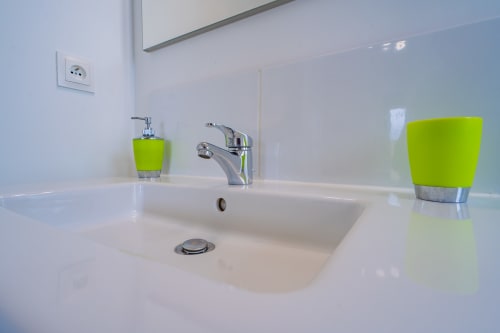 Lavabo moderne avec robinetterie chromée, plan de travail blanc et accessoires vert citron à l'appartement Room In Toulouse