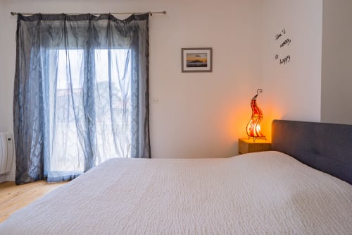 Chambre moderne dans un appartement toulousain avec vue sur la ville, lampe néon, rideaux voilages et accès balcon
