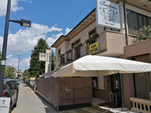 Facciata di una trattoria a Vignola con ombrello bianco, recinto marrone e insegna dell'Hotel Eden visibile