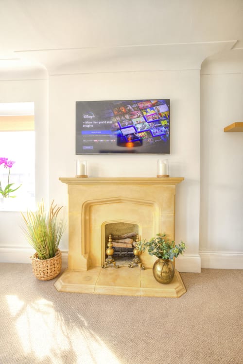 Modern fireplace with cream mantelpiece, potted plants, and wall-mounted TV displaying Disney+ streaming service in Dee-8