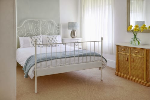Bright bedroom at Dee-8 apartment in West Kirby with white metal bed, wooden dresser, yellow flowers, and garden views