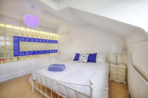 Modern bedroom at Dee-8 apartment in West Kirby with white bed, blue accents, illuminated glass blocks, and garden view