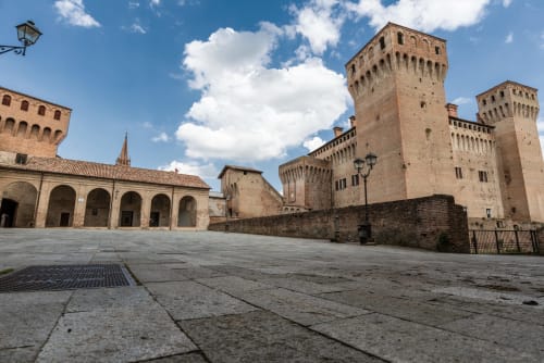 Cortile del castello medievale di Vignola con torri in pietra e portico ad archi sotto il cielo azzurro