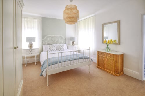 Spacious bedroom at Dee-8 hotel with white metal bed frame, woven pendant light, and natural furnishings in West Kirby.