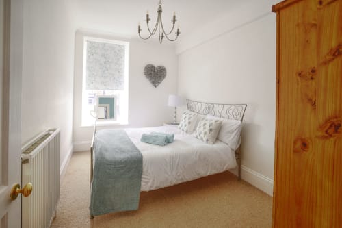 Bright bedroom at Dee-8 in West Kirby with queen bed, grey bedding, metal headboard, chandelier, and wooden wardrobe