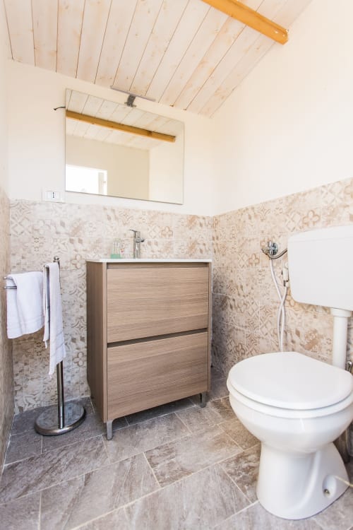 Modern bathroom in Villa Maria with wooden vanity, patterned tile walls, toilet, and wooden ceiling beams in Valderice,
