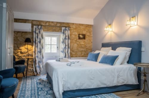 Chambre élégante au Château Haut Clarise avec lit en velours bleu, mur en pierre et équipements modernes