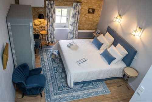 Chambre accueillante au Château Haut Clarise avec lit blanc, oreillers bleus, murs en liège et équipements modernes