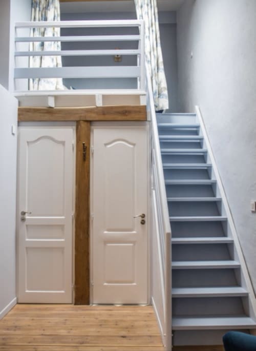 Escalier et portes crème du Château Haut Clarise, gîte français aux marches bleu-gris et finitions en bois.