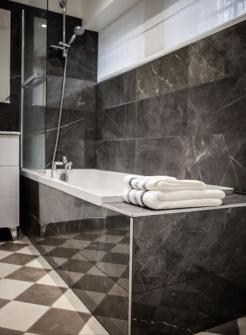 Salle de bain moderne au Château Haut Clarise avec carrelage en marbre noir, baignoire blanche, cabine de douche vitrée et serviettes roulées