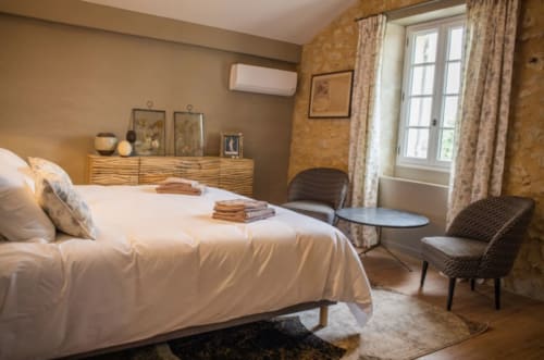 Chambre élégante du Château Haut Clarise avec lit blanc, commode en bois et portes-fenêtres à Belvès-de-Castillon