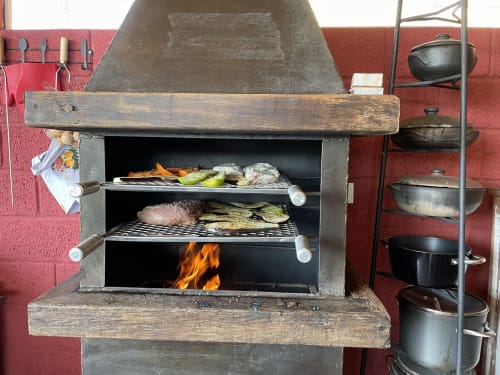 Churrasqueira tradicional a lenha com carnes e vegetais em cocção, na pousada Paraíso nas Montanhas em Campos do Jordão