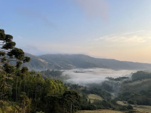 Vista da serra enevoada no vale do hotel Paraíso nas Montanhas em Campos do Jordão, com encostas florestadas e neblina matinal