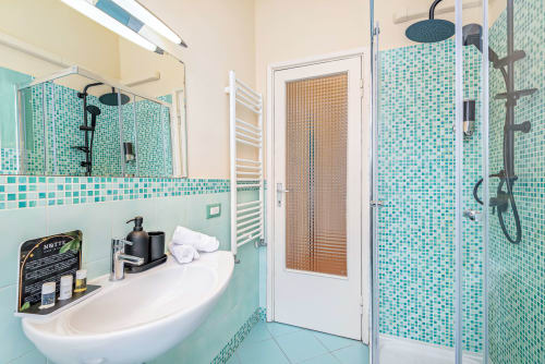 Bagno moderno turchese nella SleepWithMe B&B di Pisa con piastrelle a mosaico, doccia a pioggia e lavandino curvo