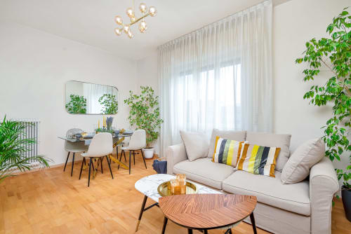 Luminoso appartamento di lusso a Pisa con divano beige, tavolo da pranzo in legno, piante in vaso e lampadario moderno