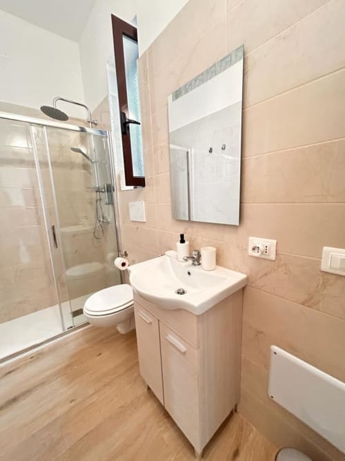 Bagno moderno dell'appartamento Newhouse a Bari con lavabo bianco, toilette, doccia a filo pavimento e pareti in piastrelle beige