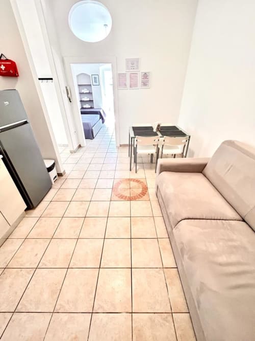 Soggiorno dell'appartamento Newhouse a Bari con divano beige, tavolo da pranzo, angolo cottura e pavimentazione in ceramica
