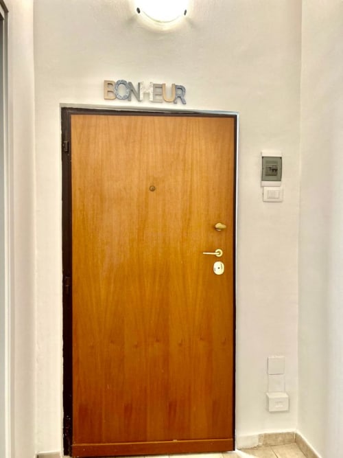 Porta in legno dell'hotel Newhouse a Bari con insegna 'BONJEUR', maniglia in ottone e montaggio a parete