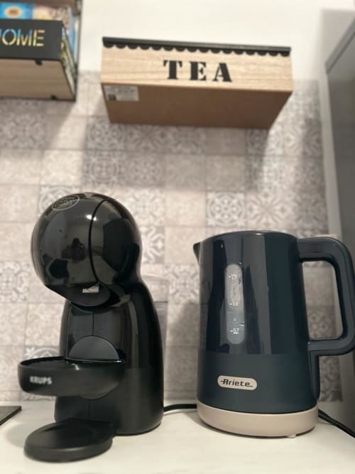 Macchinetta del caffè nera e bollitore elettrico sulla scrivania dell'appartamento Newhouse a Bari con scatola di tè sullo sfondo