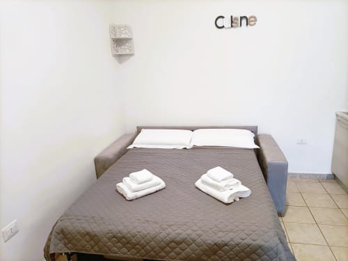 Ampia camera da letto in appartamento a Bari con letto trapuntato grigio, cuscini bianchi e set di asciugamani, muri bianchi e pavimentazione in piastrelle