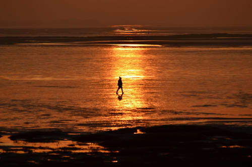 Silhouetted figure jogging on West Kirby beach at golden sunset, Merseyside