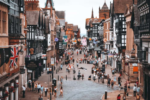 Historic Tudor-style street in Chester with red brick buildings, black and white timber frames, and crowds of visitors