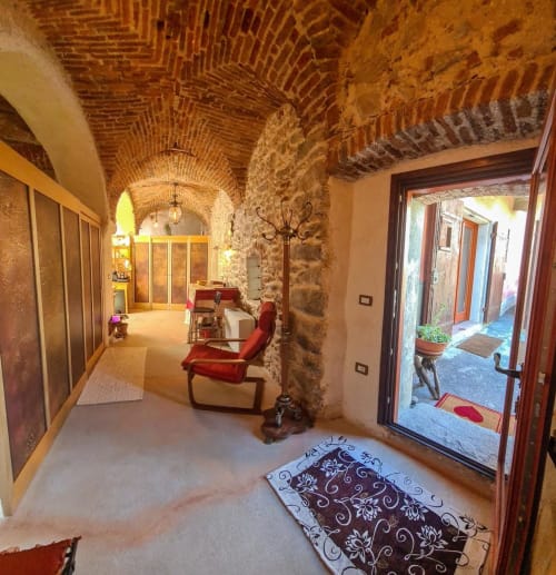 Suggestivo corridoio con volta in mattoni, sedute rosse e muratura in pietra presso la locanda CasaRosada a Vidracco, Italia