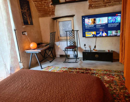 Camera CasaRosada a Vidracco con letto, scrivania, sedia, TV e muri in laterizio a vista
