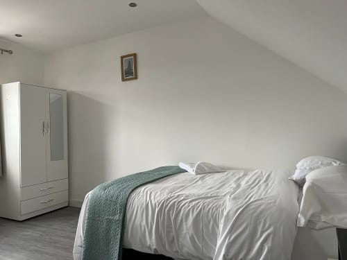Bright attic bedroom at Starlet Property London with white wardrobe, bed with teal throw, and framed wall art
