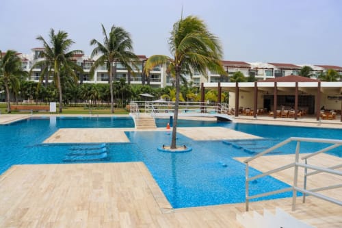 Área de piscina del Resort Mareazul en Playa del Carmen con palmeras, tumbonas y edificios con vistas al océano