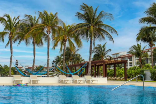 Área de piscina del Resort Mareazul con palmeras, tumbonas, toboganes y vista al océano en Playa del Carmen