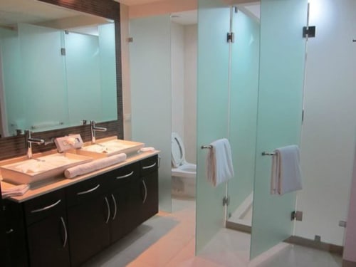 Baño moderno en Mareazul Resort Frente al Mar, Playa del Carmen, con doble lavamanos, ducha con cristal esmerilado y acabados oscuros