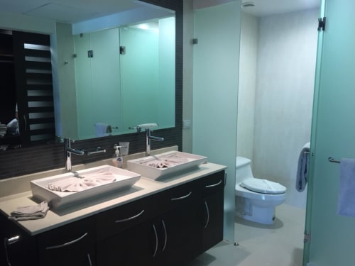 Baño moderno en Mareazul Resort Frente al Mar con doble lavamanos, vanidad negra y detalles en vidrio aguamarina en Playa del Carmen