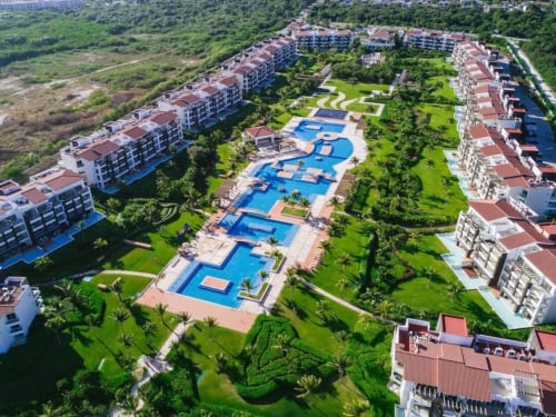 Vista aérea del resort frente al mar Mareazul con piscinas azules, jardines exuberantes y edificios con techos rojos en Playa del Carmen