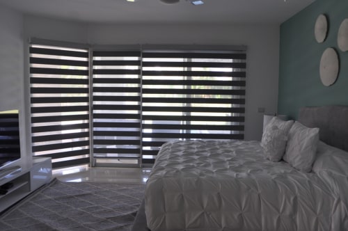 Habitación moderna en Mareazul Resort Frente al Mar con cortinas estriadas, ropa de cama gris y vista al océano en Playa del Carmen.
