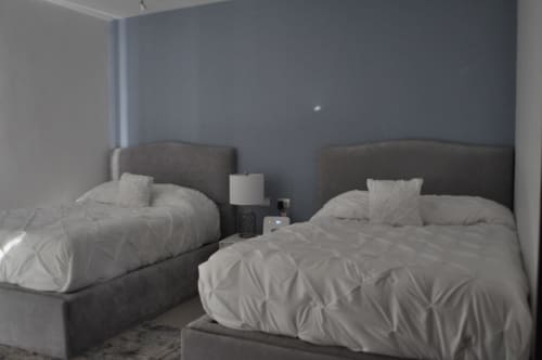 Dos camas individuales con ropa de cama blanca y cabeceros grises en una habitación del moderno Resort Mareazul Beachfront, Playa del Carmen.
