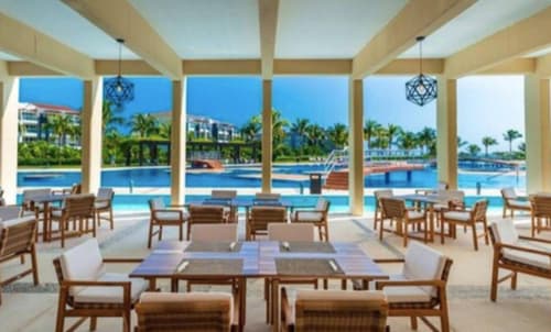 Área de comedor del Mareazul Beachfront Resort con vistas al océano, sillas de madera y palmeras en Playa del Carmen