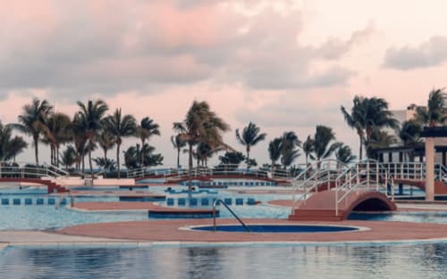Vibrante área de piscina del Resort Mareazul con palmeras y vistas al océano en Playa del Carmen