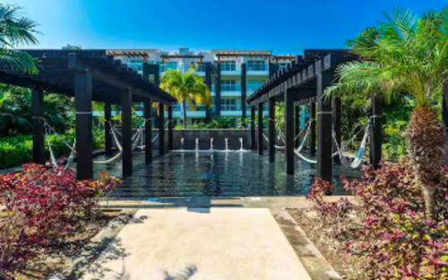 Paseo frente al mar del Mareazul Beachfront Resort con pérgolas negras, flores tropicales y vista al agua azul en Playa del