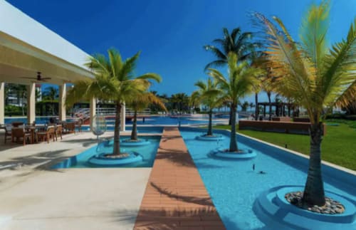 Piscina con terraza azul del Resort Mareazul, rodeada de palmeras, pasarelas de madera y vistas frente al mar en Playa del Carmen
