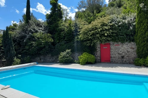 Piscine bleu vif au Mas de Trépeloup à Alès, France, entourée de verdure luxuriante et de murs en pierre