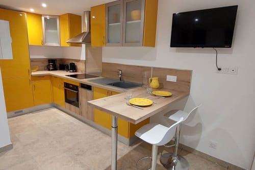 Cuisine moderne avec armoires jaunes, plan de travail en bois, salle à manger et TV au Mas de Trépeloup BnB à Alès