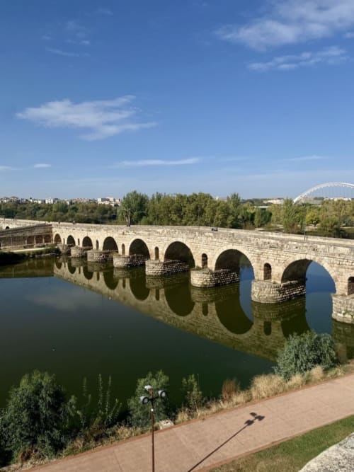 Antiguo puente de piedra cruzando el río en Mérida, España con vegetación exuberante y cielo azul despejado