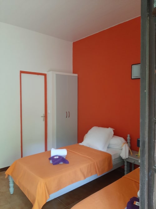Modern bedroom at Mon Refuge hotel with orange accent wall, single bed, wardrobe, and door in Les Anses d'Arlet