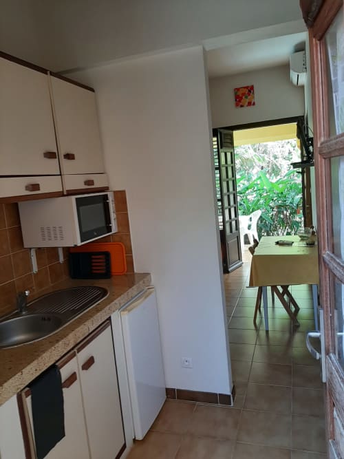 Compact kitchen in Serenity apartment at Mon Refuge hotel, Martinique, with white cabinets, microwave, and garden view access