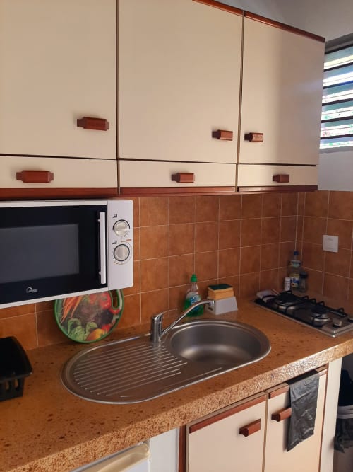 Compact kitchen in Serenity apartment at Mon Refuge hotel, Martinique, with microwave, gas stovetop, and brown tile